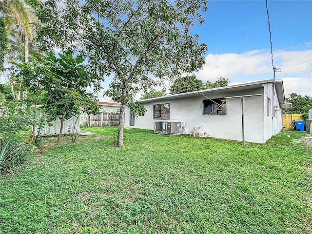 back of property featuring a lawn, cooling unit, fence, and stucco siding