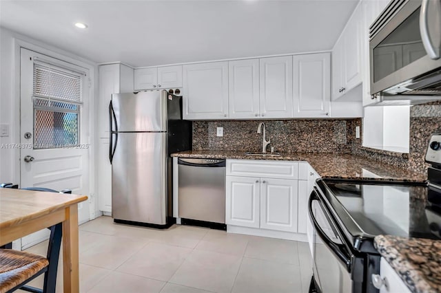 kitchen with dark stone countertops, light tile patterned floors, white cabinetry, stainless steel appliances, and tasteful backsplash