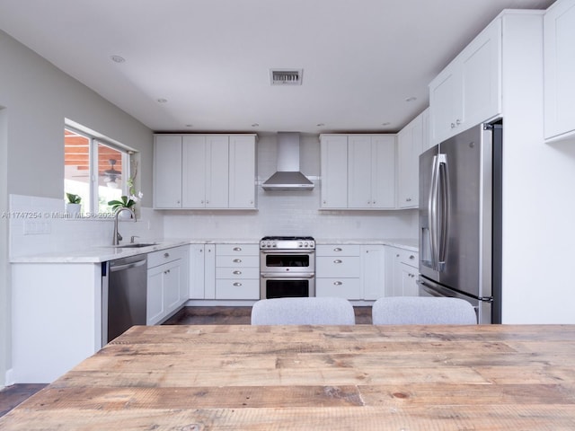 kitchen with appliances with stainless steel finishes, wall chimney range hood, decorative backsplash, sink, and white cabinetry