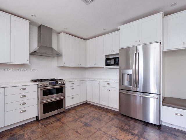 kitchen featuring light stone counters, white cabinetry, stainless steel appliances, wall chimney exhaust hood, and decorative backsplash