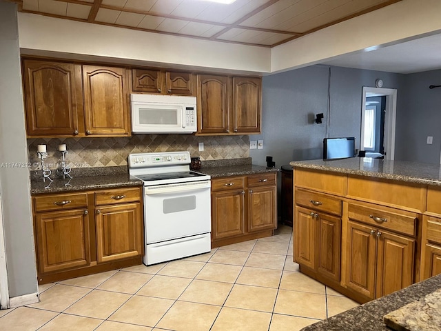 kitchen featuring light tile patterned flooring, white appliances, dark stone countertops, and backsplash