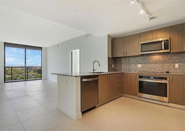 kitchen with appliances with stainless steel finishes, a sink, stone counters, decorative backsplash, and a peninsula