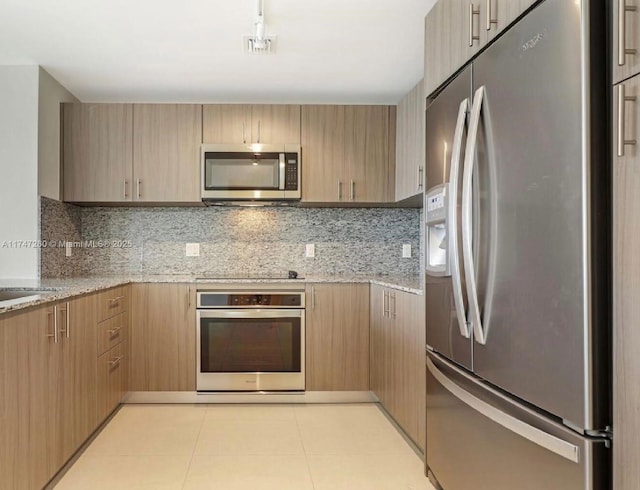 kitchen with stainless steel appliances, tasteful backsplash, light stone counters, and light brown cabinetry