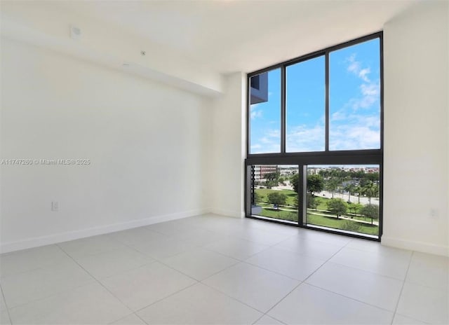 tiled empty room featuring floor to ceiling windows and baseboards