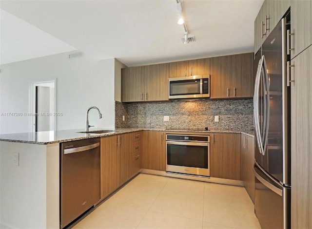 kitchen with kitchen peninsula, sink, stone counters, appliances with stainless steel finishes, and decorative backsplash