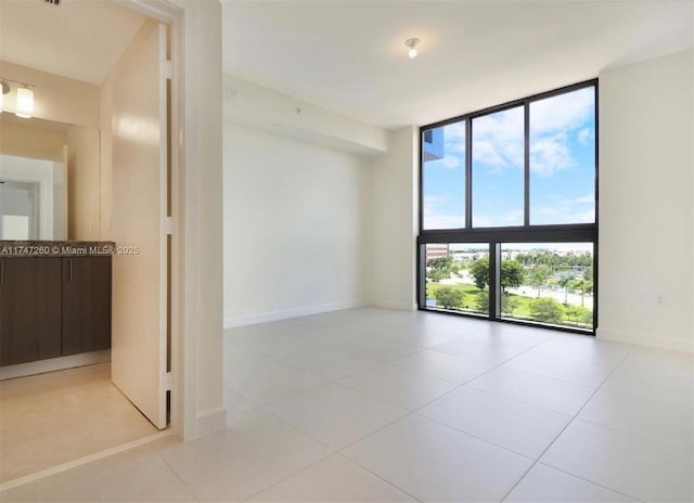 spare room with expansive windows, tile patterned floors, and baseboards