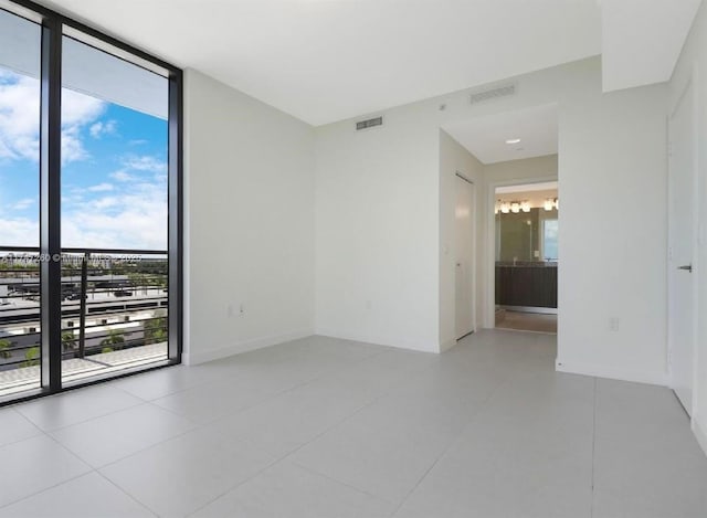 spare room featuring expansive windows, light tile patterned floors, and baseboards
