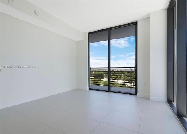 unfurnished room with floor to ceiling windows, baseboards, light tile patterned flooring, and a smoke detector