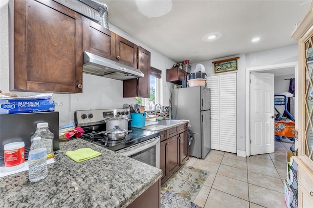 kitchen with light tile patterned floors, dark brown cabinetry, appliances with stainless steel finishes, light stone countertops, and under cabinet range hood