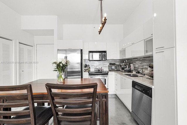 kitchen with stainless steel appliances, concrete floors, backsplash, sink, and white cabinetry