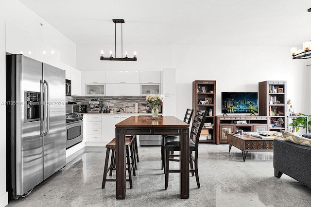 kitchen with a notable chandelier, tasteful backsplash, appliances with stainless steel finishes, white cabinets, and pendant lighting