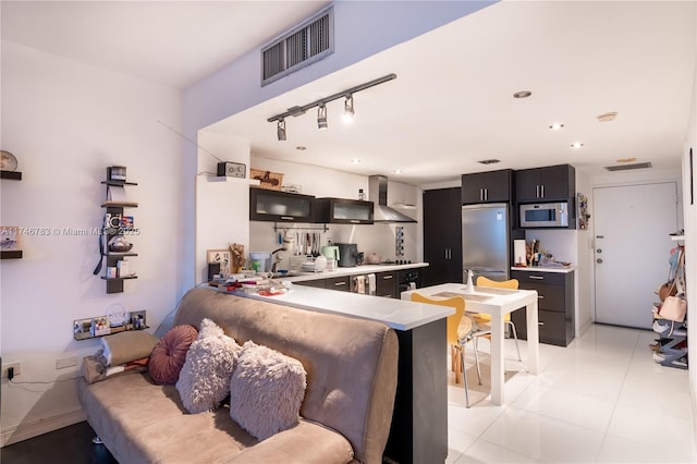 kitchen featuring visible vents, dark cabinets, stainless steel appliances, wall chimney range hood, and a sink