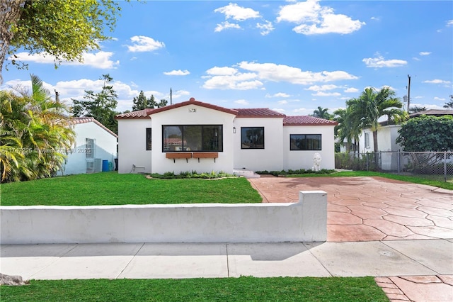 mediterranean / spanish-style home featuring a tiled roof, a front yard, fence, and stucco siding