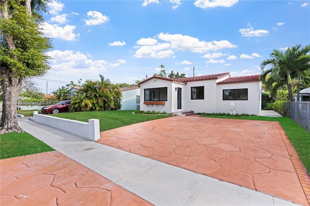 mediterranean / spanish-style house with a tile roof, fence, a front yard, stucco siding, and a patio area