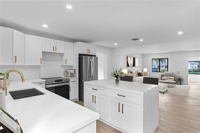 kitchen featuring a center island, stainless steel appliances, open floor plan, white cabinetry, and a sink