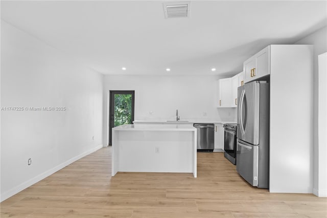 kitchen with light countertops, appliances with stainless steel finishes, white cabinets, a kitchen island, and a sink