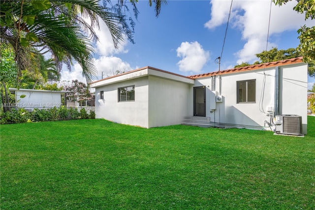 rear view of house featuring a lawn, central AC, and stucco siding