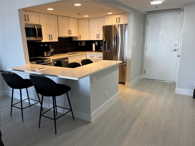 kitchen with appliances with stainless steel finishes, sink, white cabinetry, a kitchen breakfast bar, and kitchen peninsula