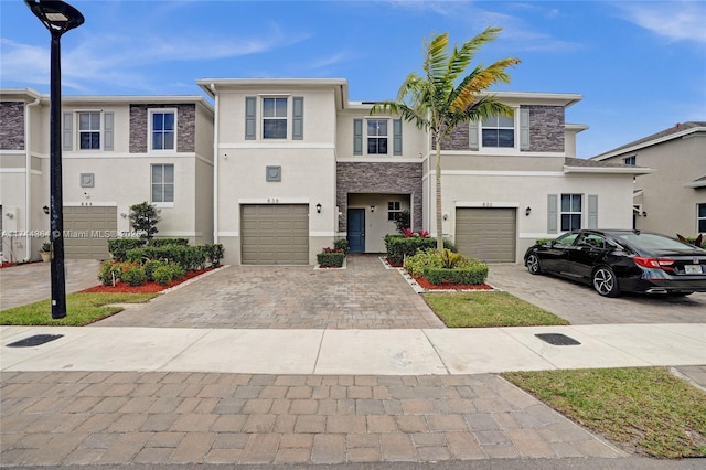 townhome / multi-family property featuring a garage, stone siding, decorative driveway, and stucco siding