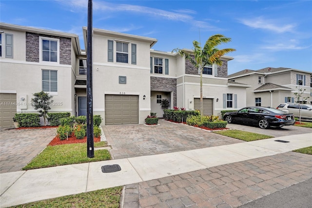 multi unit property with decorative driveway, stucco siding, a garage, a residential view, and stone siding