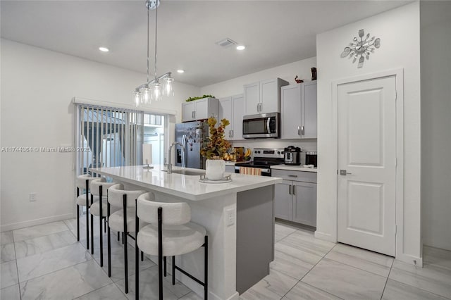 kitchen featuring a kitchen breakfast bar, decorative light fixtures, a kitchen island with sink, stainless steel appliances, and a sink