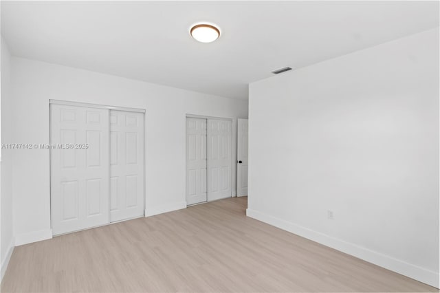 unfurnished bedroom with light hardwood / wood-style floors and multiple closets