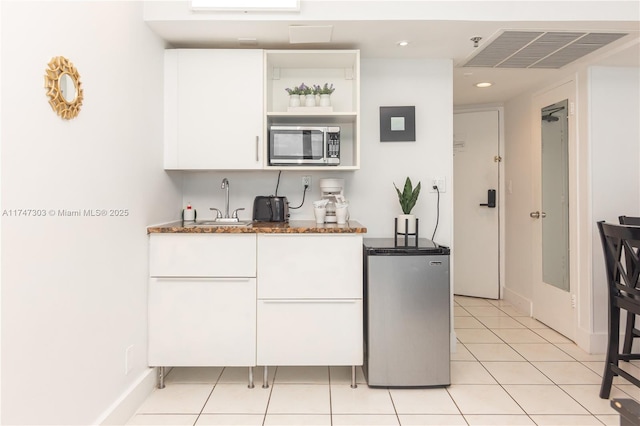 kitchen featuring sink, light tile patterned flooring, dark stone counters, stainless steel appliances, and white cabinets