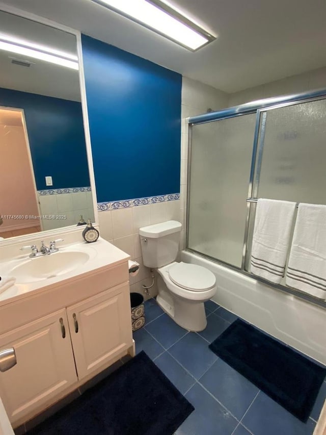 full bathroom with tile patterned flooring, toilet, tile walls, enclosed tub / shower combo, and vanity