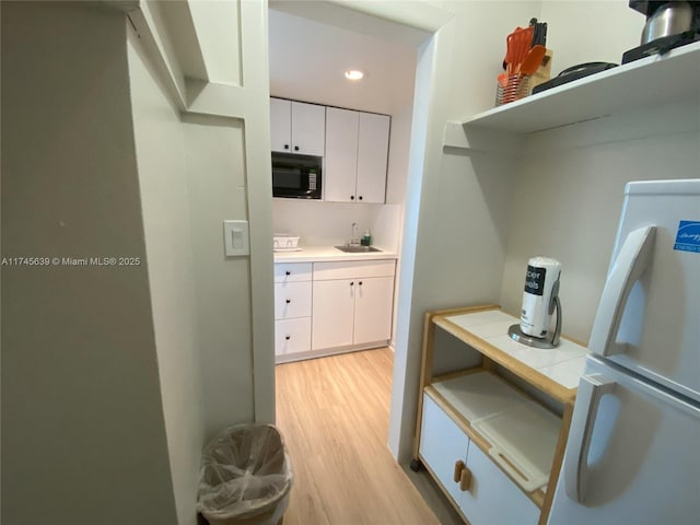 kitchen with white fridge, sink, white cabinetry, and light wood-type flooring