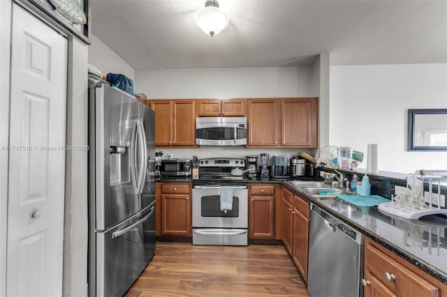 kitchen featuring appliances with stainless steel finishes, sink, dark stone counters, and dark wood-type flooring