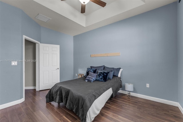 bedroom with dark hardwood / wood-style flooring, ceiling fan, and a tray ceiling