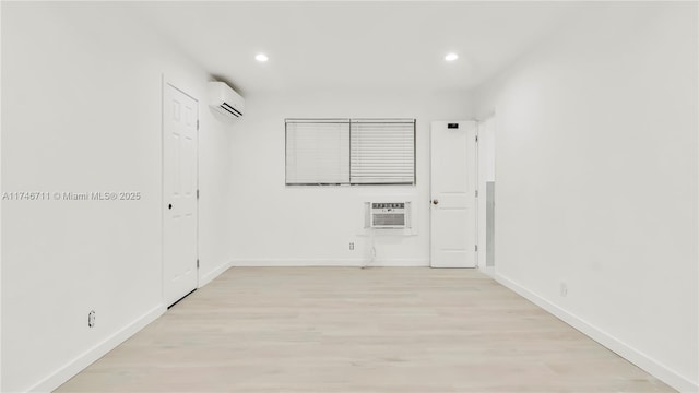 unfurnished room featuring light wood finished floors, baseboards, an AC wall unit, and a wall mounted air conditioner