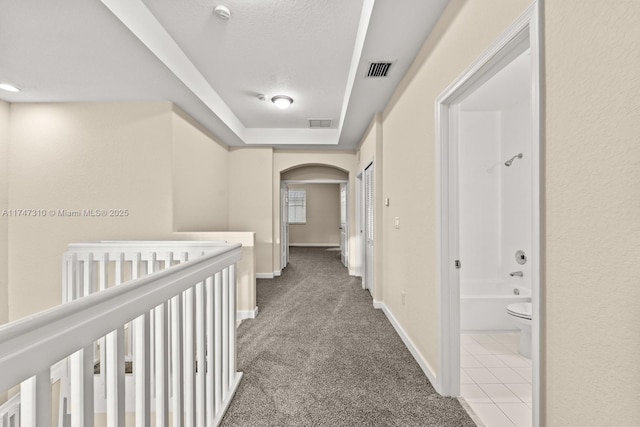 corridor with a raised ceiling, light carpet, and a textured ceiling