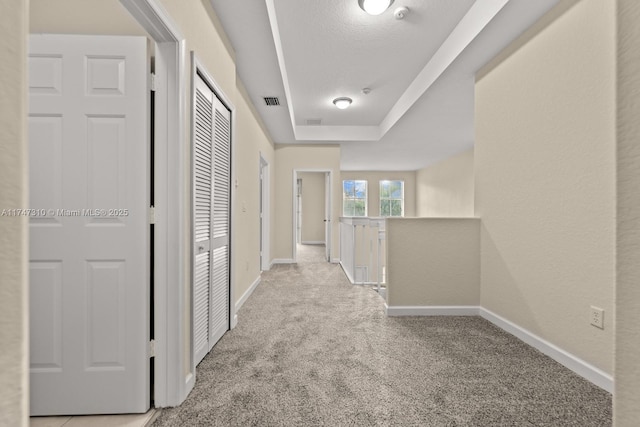 hallway with light carpet, a tray ceiling, and a textured ceiling