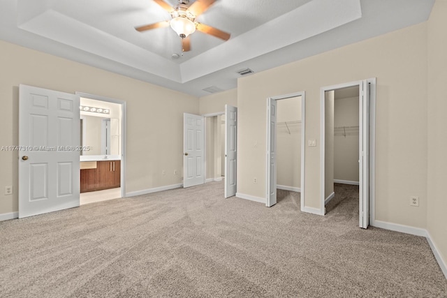 unfurnished bedroom with a tray ceiling, light carpet, ensuite bathroom, and ceiling fan