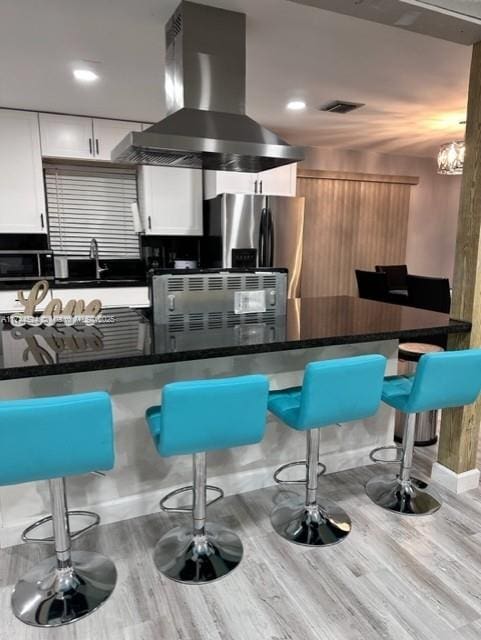 kitchen with light hardwood / wood-style flooring, white cabinetry, a breakfast bar area, and island exhaust hood