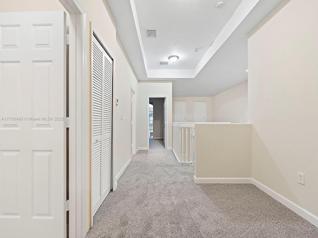 corridor featuring a tray ceiling and light carpet