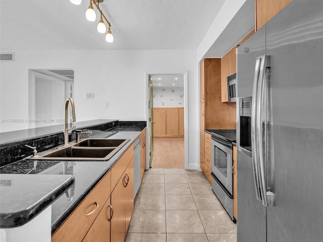 kitchen featuring sink, dark stone counters, stainless steel appliances, and light tile patterned floors