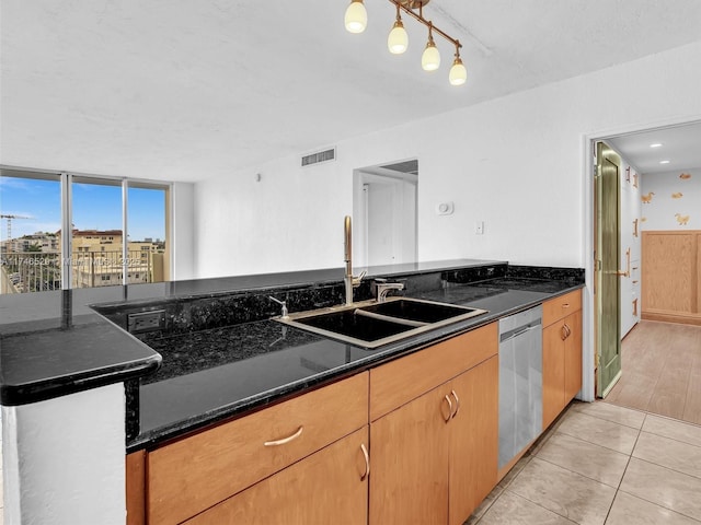 kitchen with sink, light tile patterned floors, dark stone counters, and dishwasher