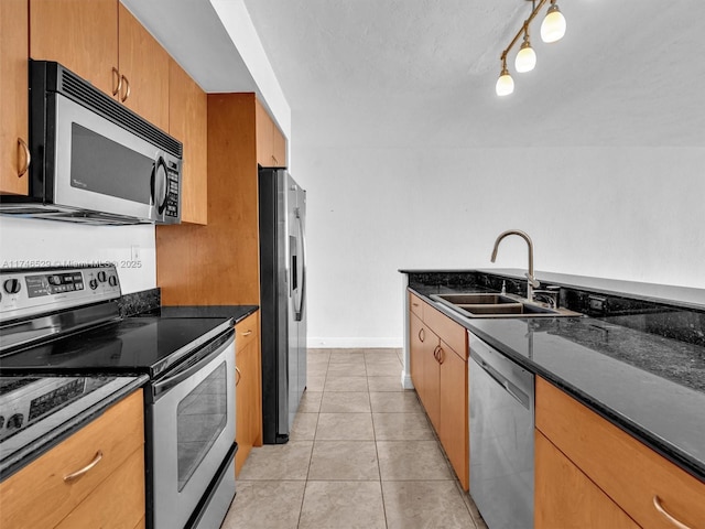 kitchen featuring dark stone countertops, light tile patterned floors, stainless steel appliances, and sink