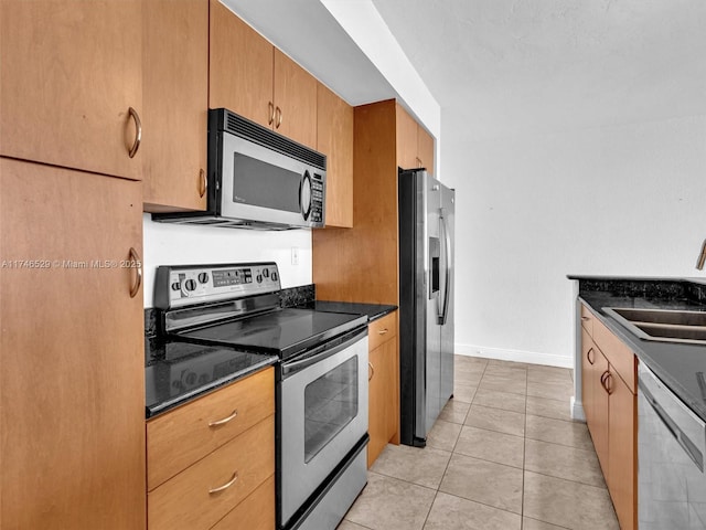 kitchen with light tile patterned floors, stainless steel appliances, dark stone counters, and sink