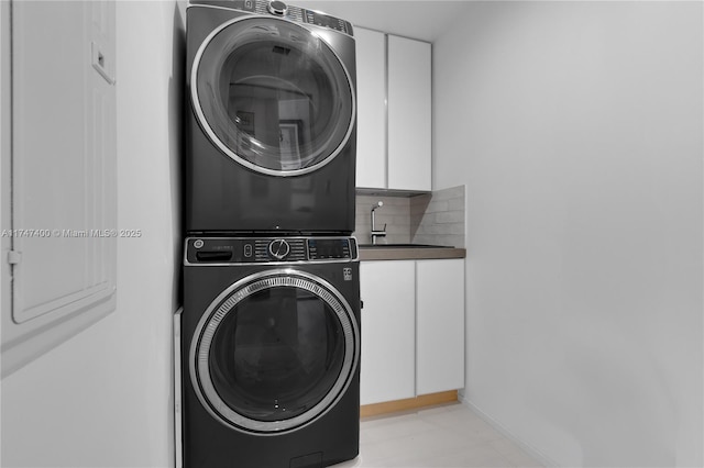 laundry room with sink, stacked washer / dryer, and cabinets