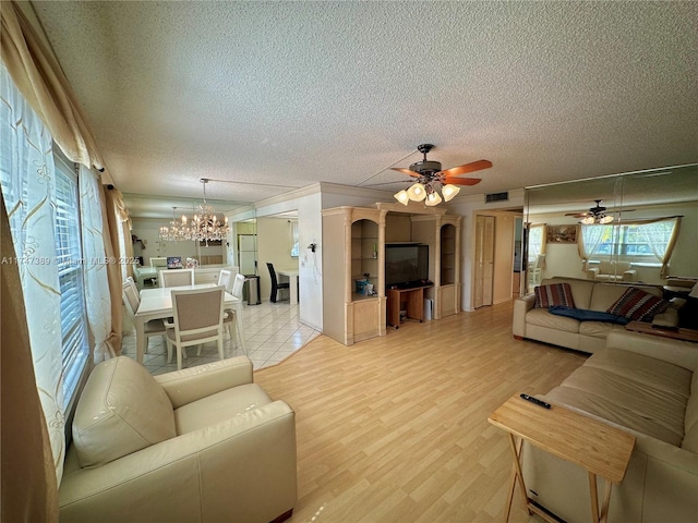 living room with visible vents, light wood-style flooring, ornamental molding, a textured ceiling, and ceiling fan with notable chandelier