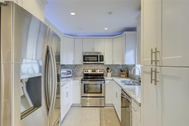 kitchen featuring white cabinets, stainless steel appliances, light stone countertops, and sink