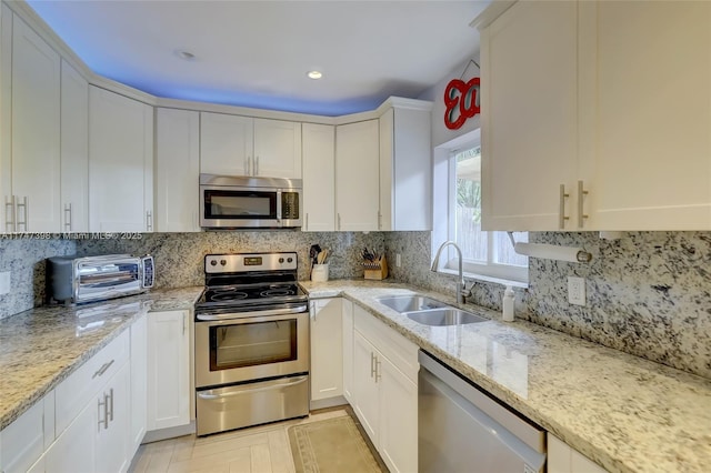 kitchen featuring appliances with stainless steel finishes, light stone countertops, white cabinets, backsplash, and sink