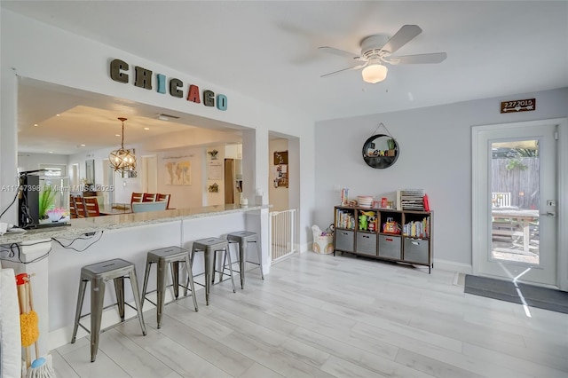 kitchen with light wood-type flooring, kitchen peninsula, pendant lighting, a kitchen bar, and ceiling fan with notable chandelier