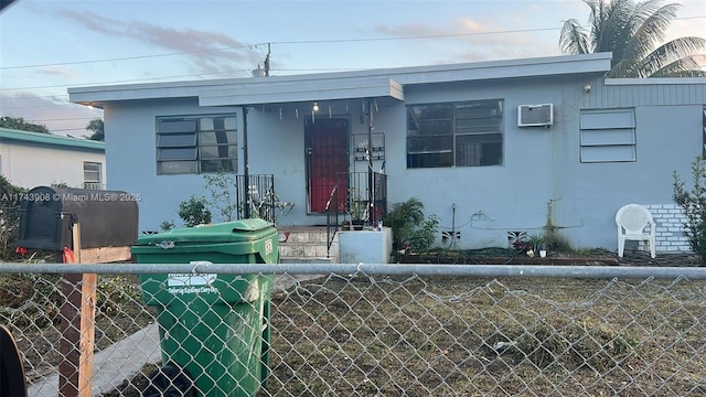 bungalow-style house with stucco siding, an AC wall unit, and fence