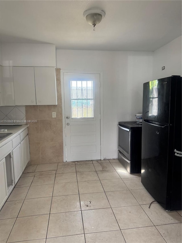 kitchen featuring light tile patterned floors, stainless steel electric range, white cabinetry, and freestanding refrigerator