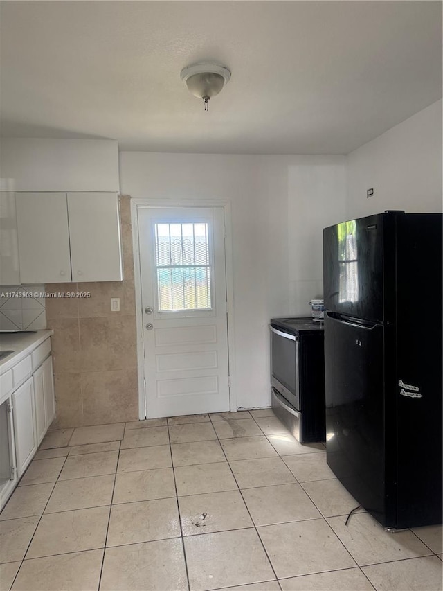 kitchen featuring light tile patterned flooring, white cabinets, stainless steel electric range, and freestanding refrigerator