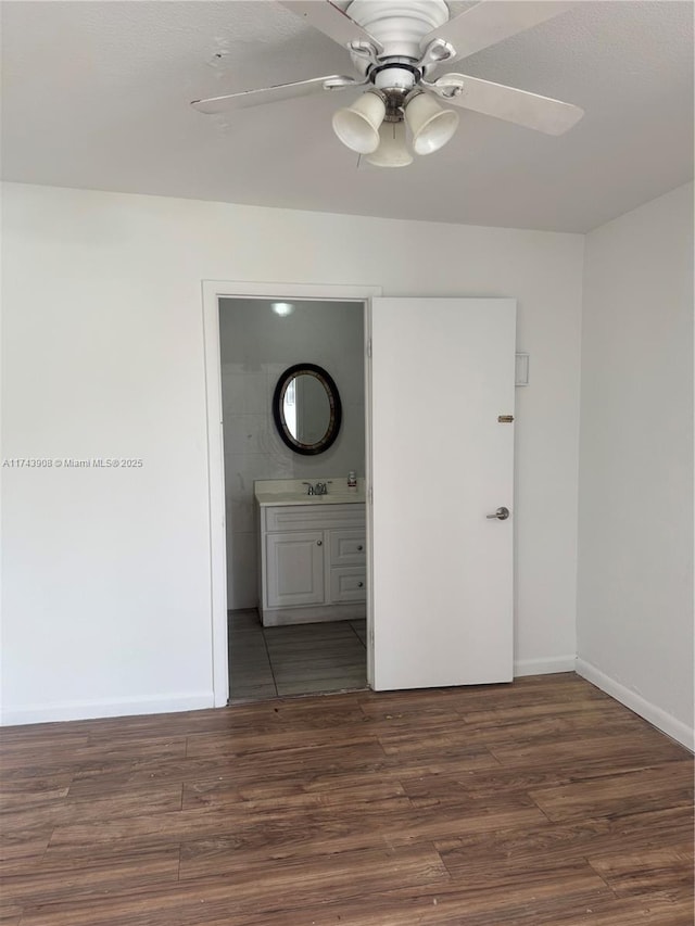 interior space featuring baseboards, ensuite bath, wood finished floors, and a ceiling fan